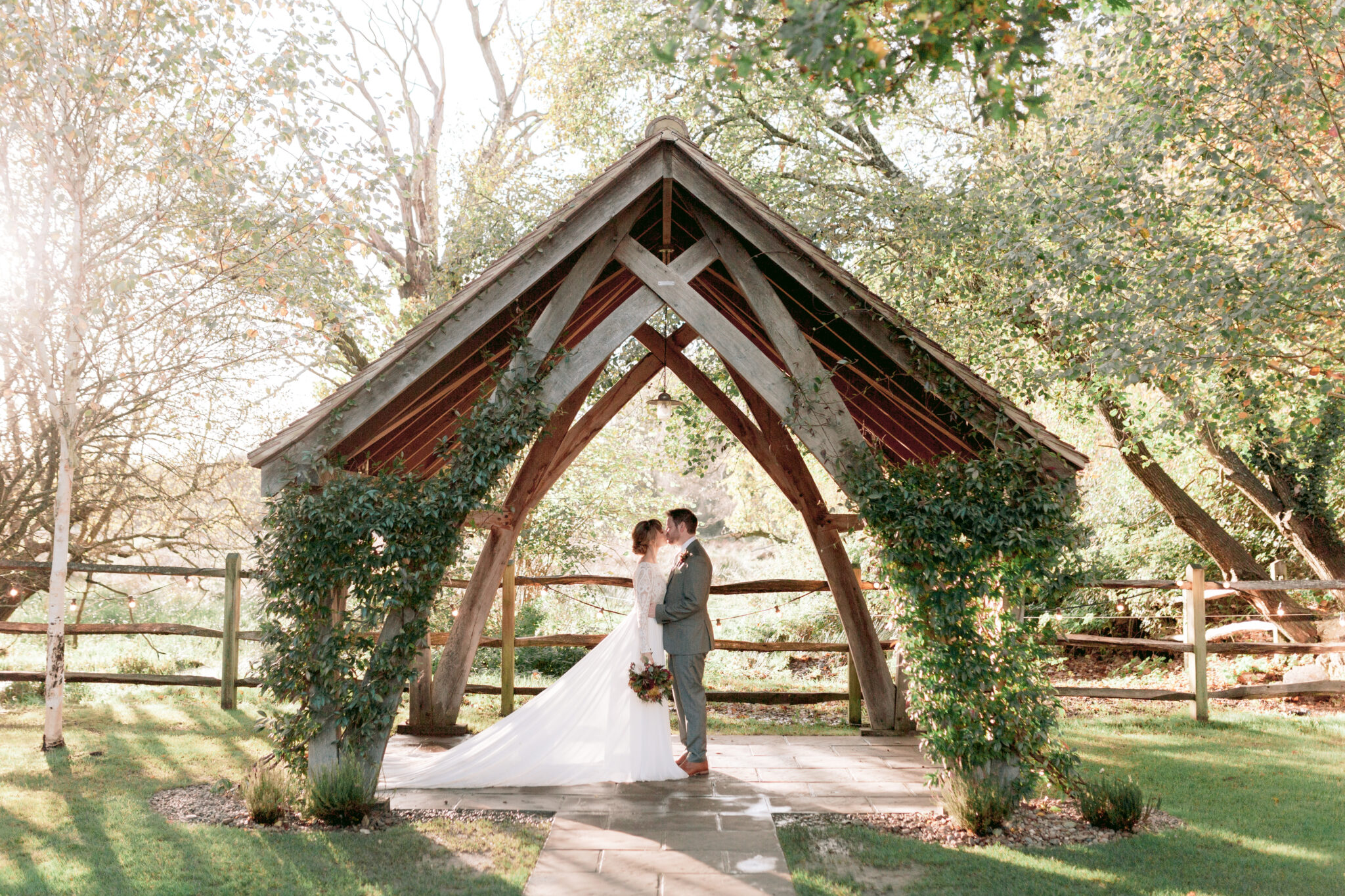 CD - By Catherine Carter Weddings-105 Couple share a kiss under the arbour at their autumnal wedding at Millbridge Court in Surrey.