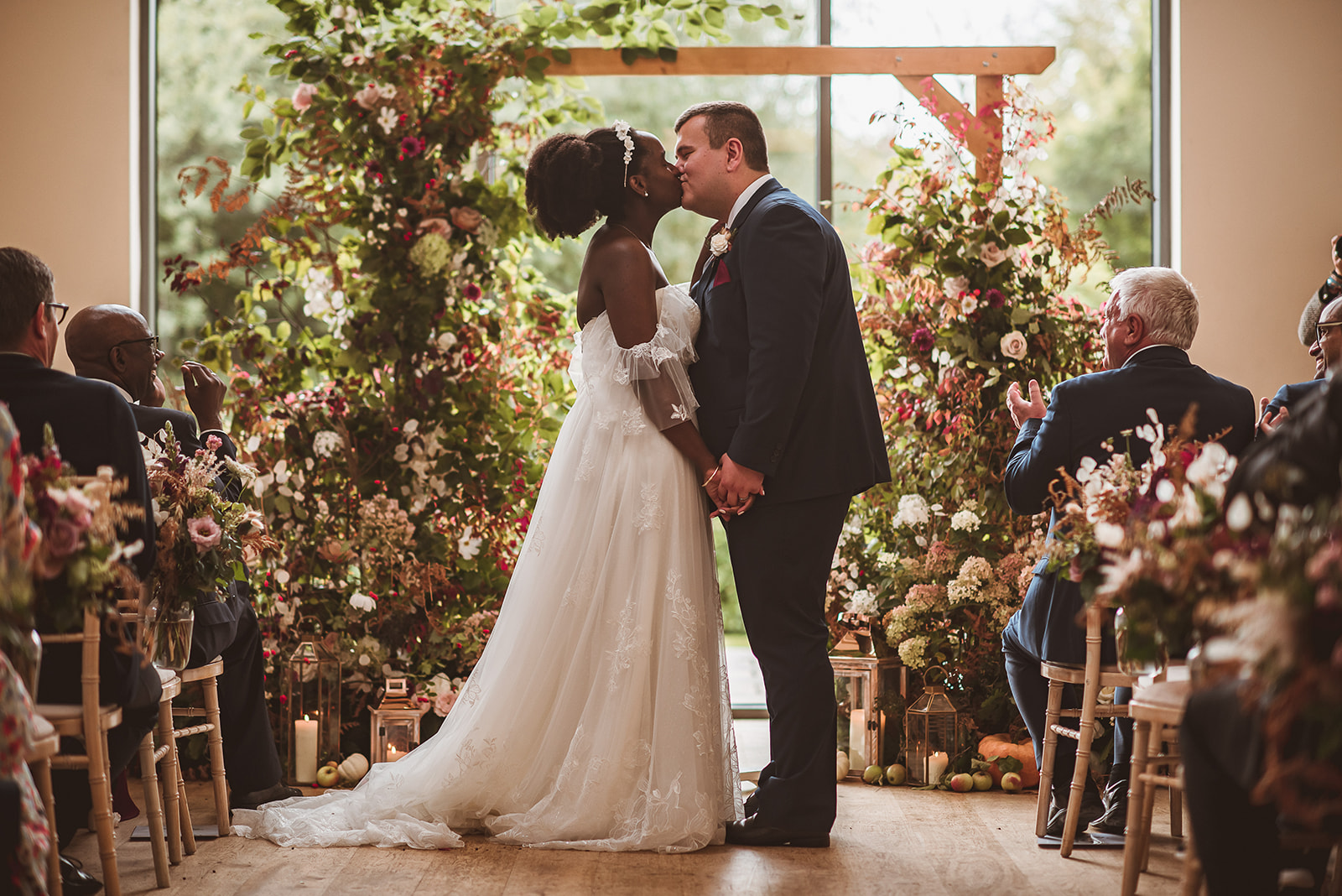 newly wed couple, share a kiss in front of an arch of flowers